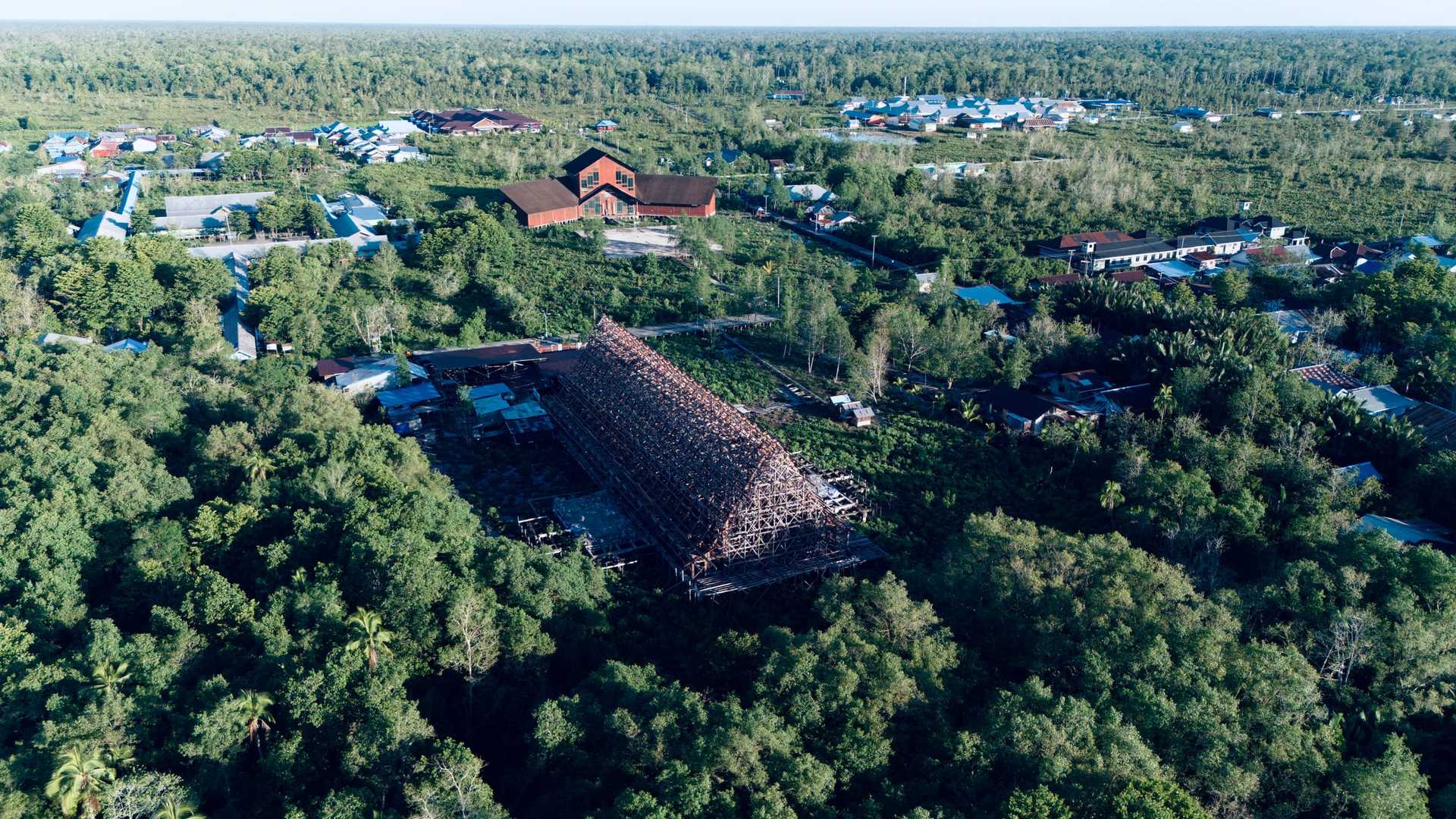 The timber frame of the new Cathedral of the Holy Cross seen from the air, roof battens in place, among the forest and houses of Agats