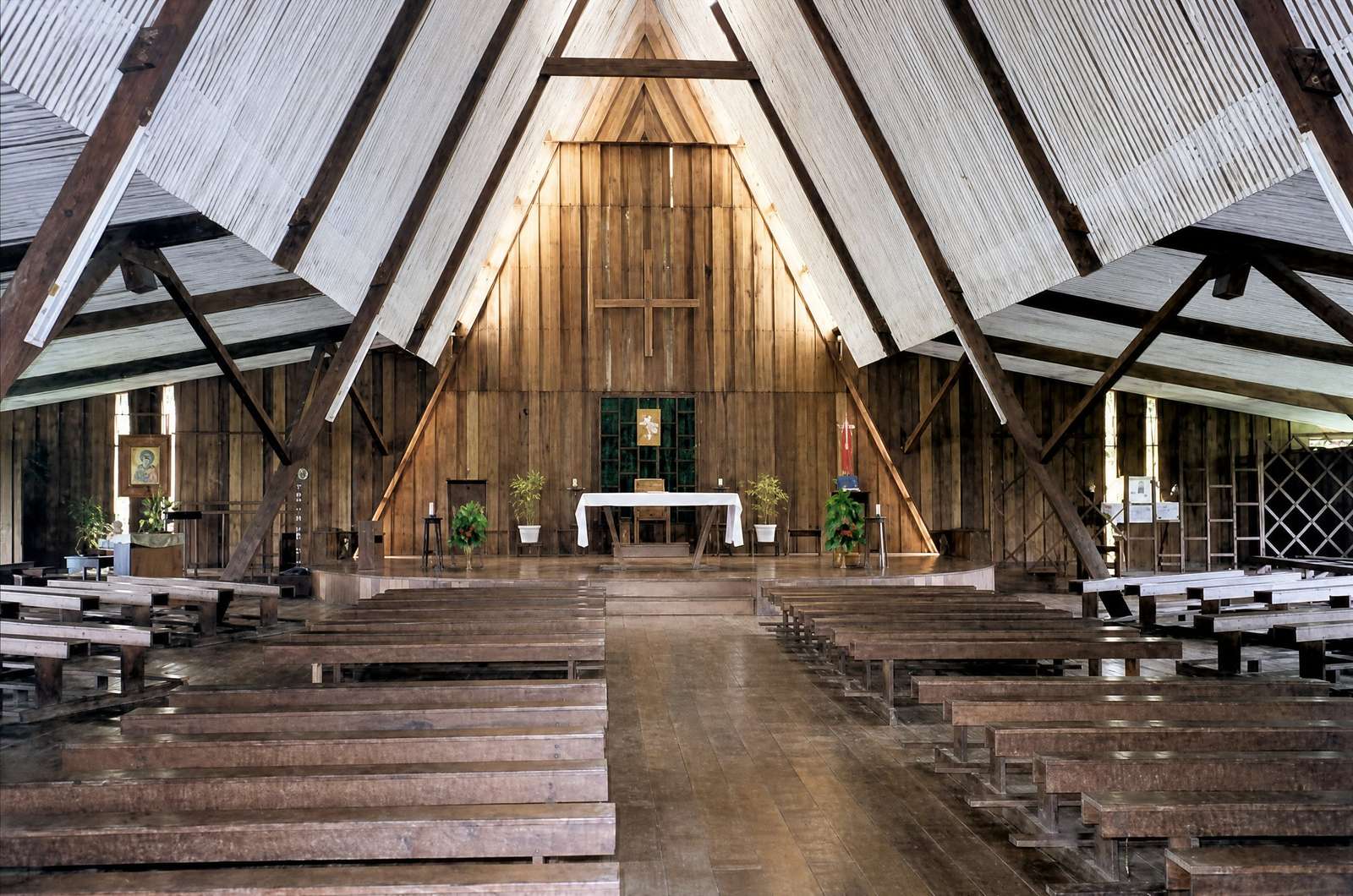 Inside the cathedral when it was new: empty pews, a plain wooden cross on the plank wall and a simple altar