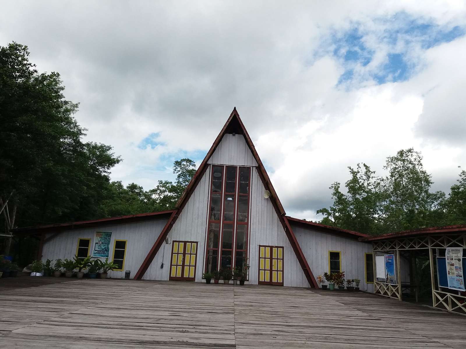 Fasad katedral yang dipakai sekarang: atap pelana putih dengan jendela tegak, pintu kuning, dan titian kayu di depannya