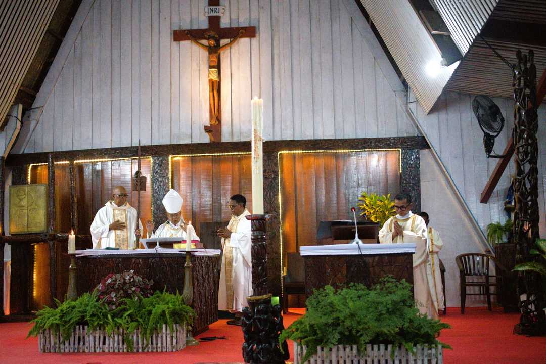 Seorang uskup mengenakan mitra di altar bersama dua pastor, dan seorang diakon di ambo