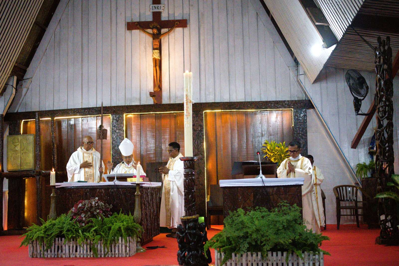 A bishop in his mitre at the altar with two priests, and a deacon at the ambo