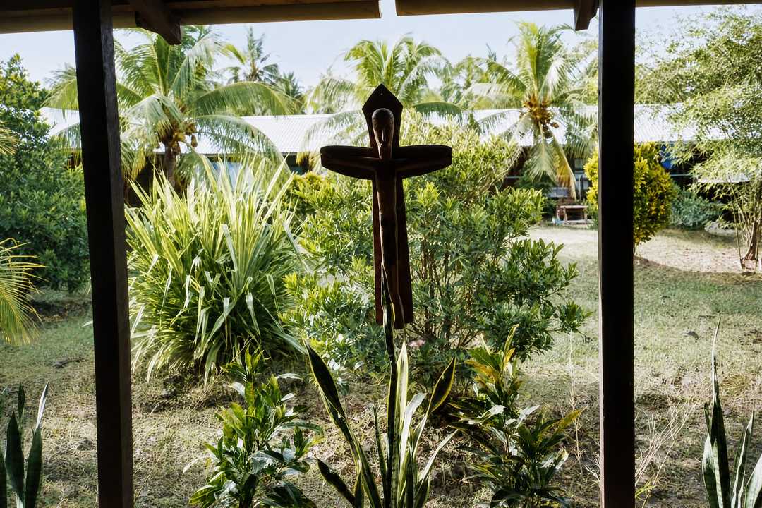 A dark wooden cross in a tropical garden, seen through a window frame